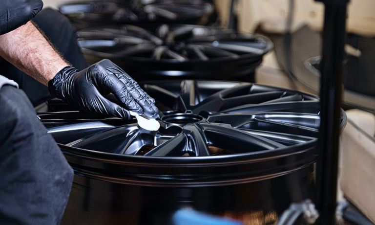 Auto detailing specialist applying premium ceramic coating to custom wheels for a glossy, protective finish.